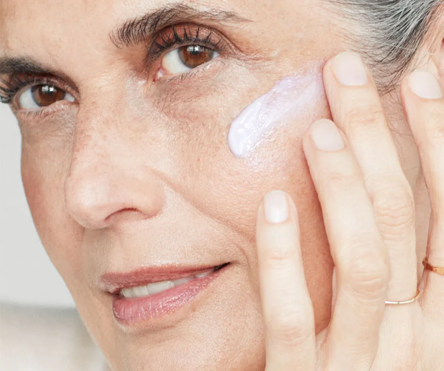 A close-up of a woman applying cream to her cheek, highlighting skincare routine.