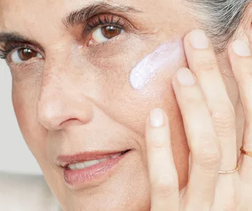 A close-up of a woman applying cream to her cheek, highlighting skincare routine.