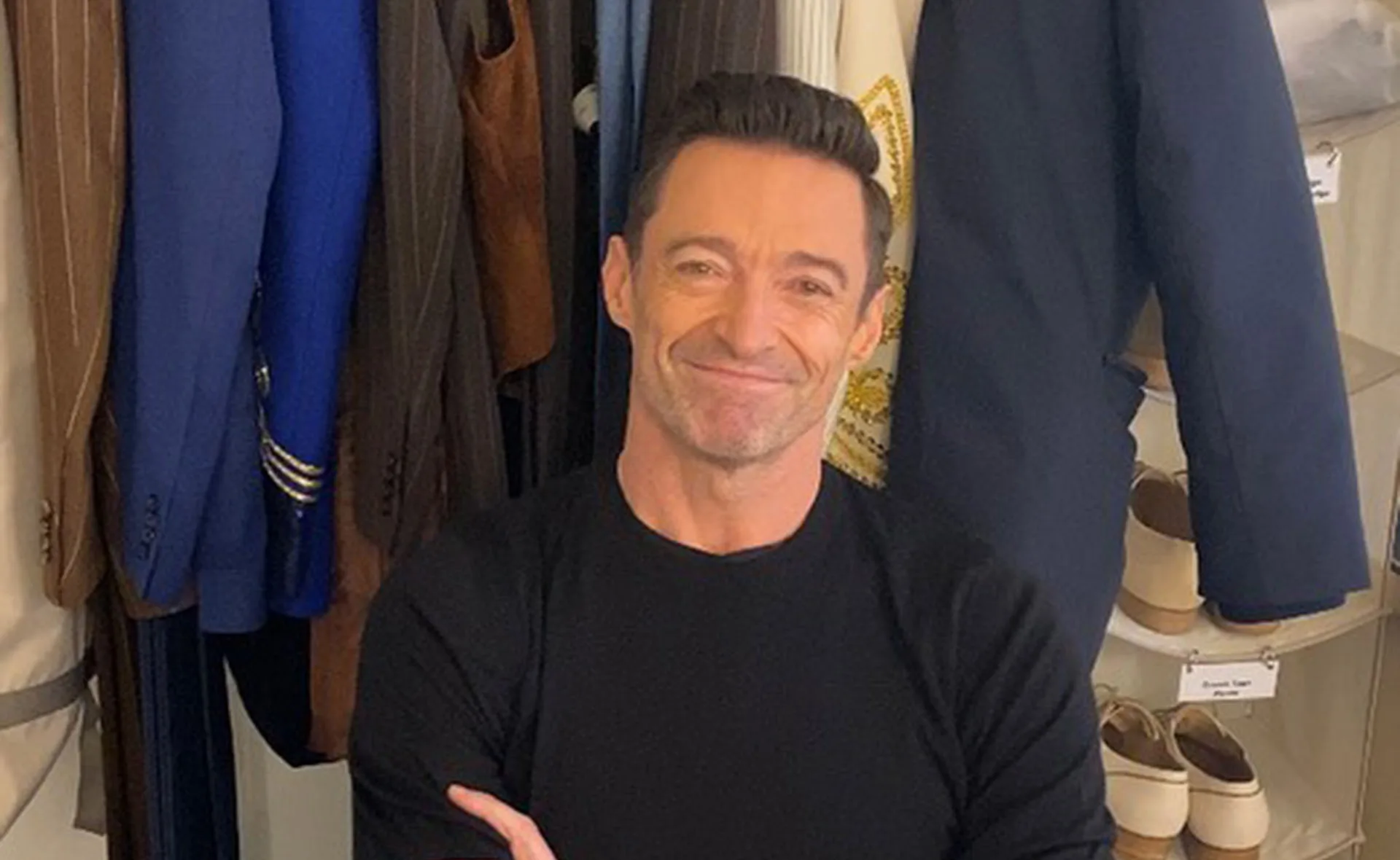 Individual smiling in a dressing room with blue, brown suits behind them.