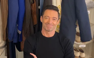 Individual smiling in a dressing room with blue, brown suits behind them.