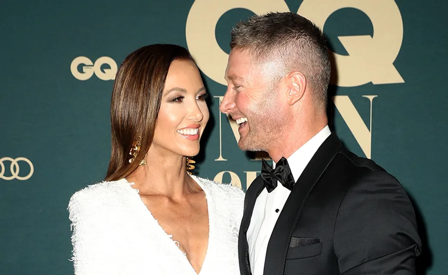 A smiling couple dressed formally, standing closely, with a GQ logo in the background.