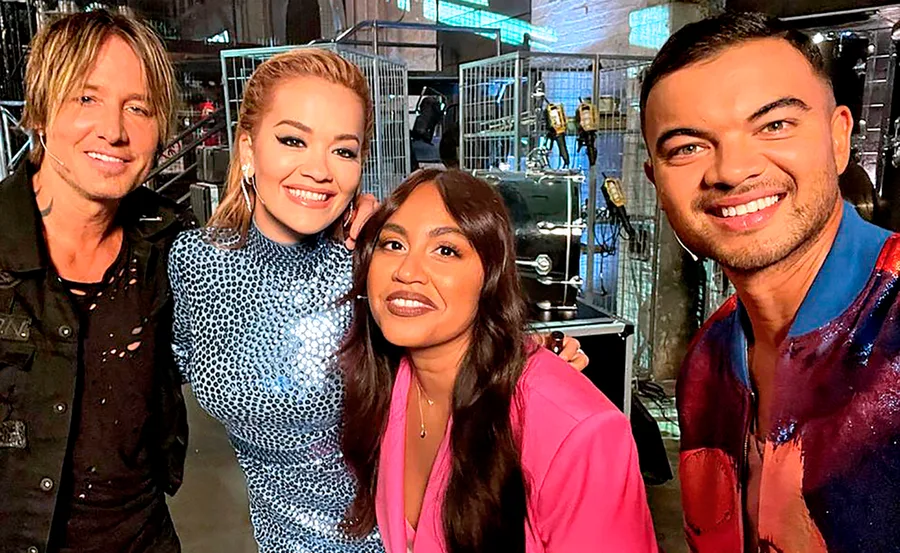 A group of four judges from "The Voice" standing together backstage, smiling at the camera.