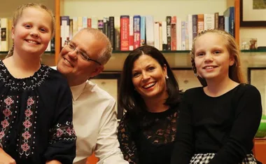 A family of four smiling in a cozy library setting with books on shelves behind them.