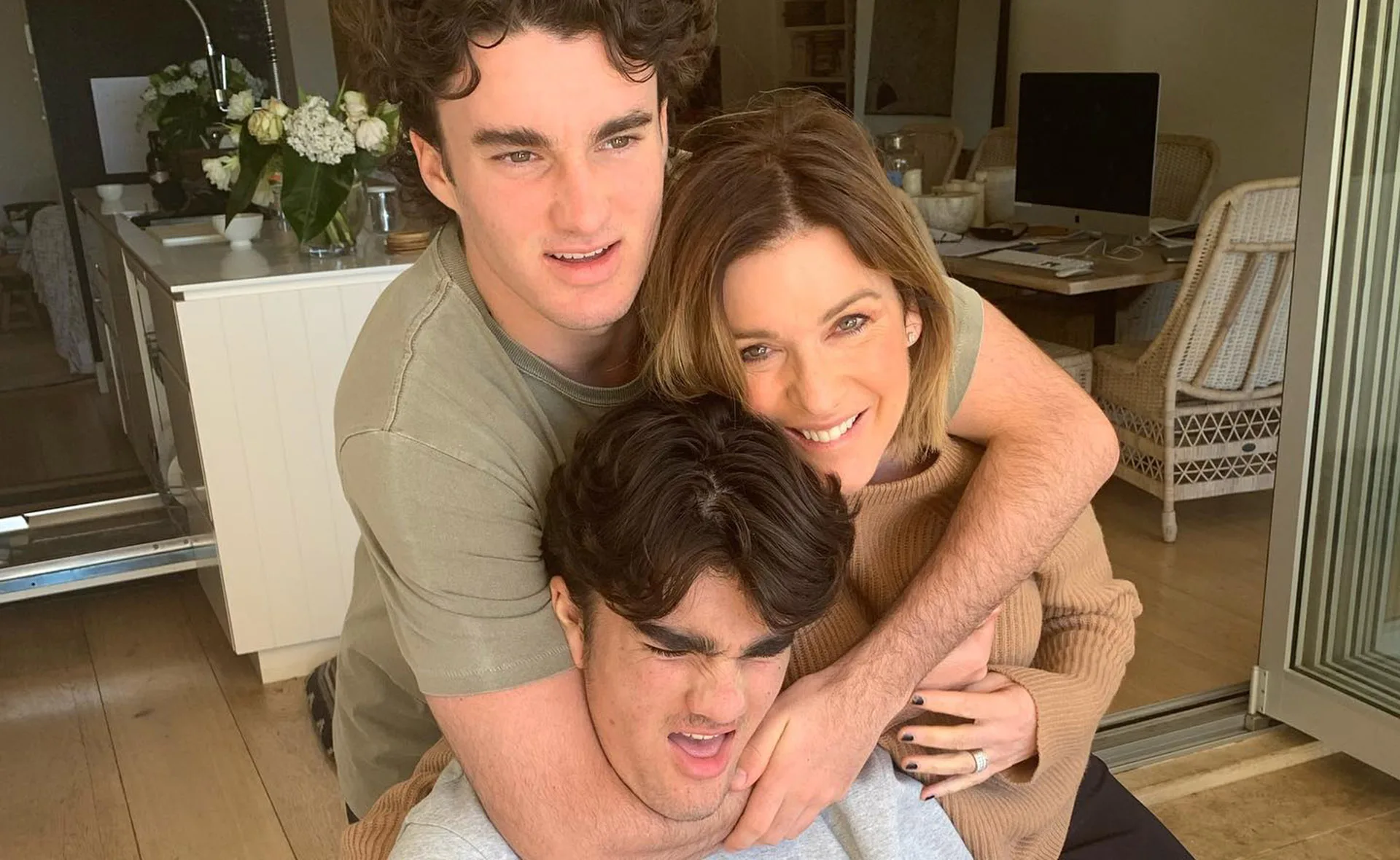 Family group hug with three people smiling in a cozy dining area.