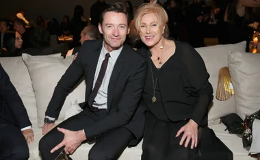 A couple sits close on a couch at a social event, smiling warmly at the camera.