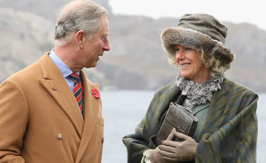 Prince Charles and Camilla smile and walk together outdoors during a royal tour in Canada.