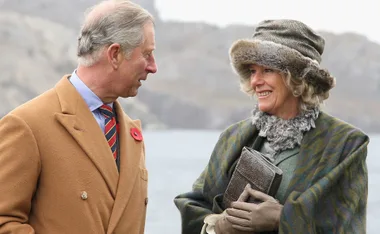 Prince Charles and Camilla smile and walk together outdoors during a royal tour in Canada.