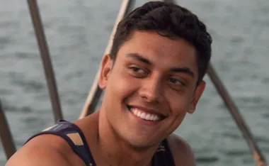 A smiling person on a boat, wearing a striped tank top, with water in the background.