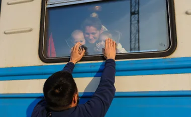 Man touches train window saying goodbye to woman and children inside.