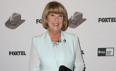 Smiling woman in light blue suit poses in front of Foxtel backdrop at an event.