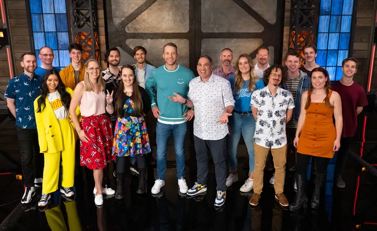 Group photo of 20 adults standing on a set with colorful attire, smiling at the camera.