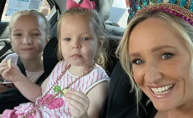 Woman wearing a crown smiles with two young girls in a car.