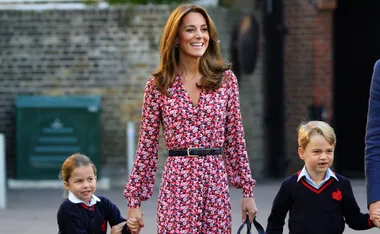 Kate Middleton with her children, Prince George and Princess Charlotte, walking outdoors, smiling, and holding hands.