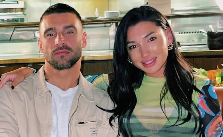 Two people are sitting closely together in a restaurant, smiling at the camera.