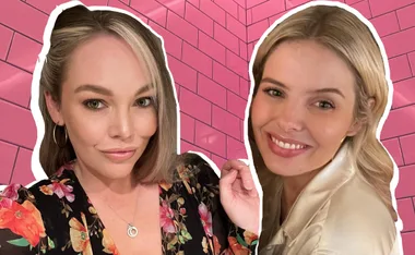 Two women smiling against a pink tiled background, one wearing floral, the other in a satin top.