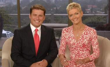 Two people sitting together, one in a suit with a red tie, and the other in a red patterned dress, both smiling.