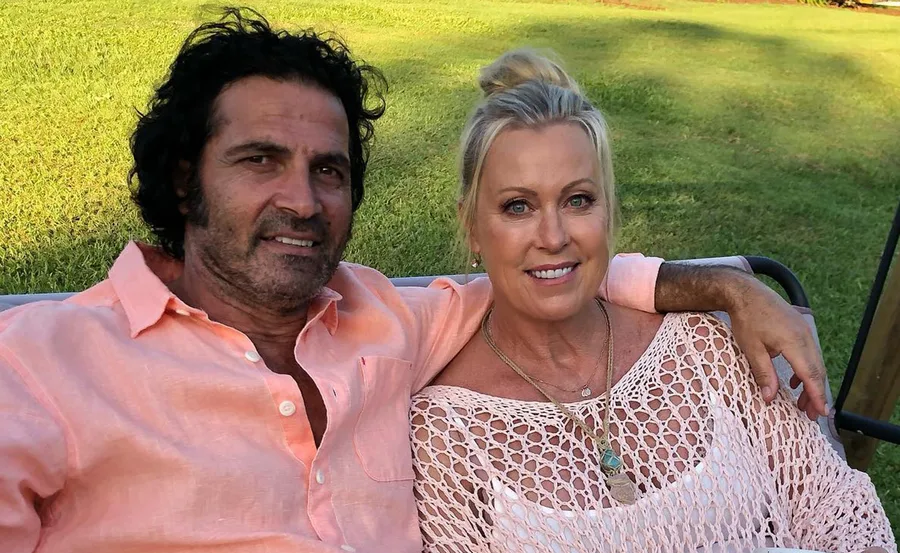 A couple sitting on a bench outdoors, smiling at the camera, with green grass in the background.