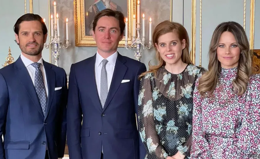 A group of four people dressed formally, smiling in a decorated room with candles and a portrait behind them.
