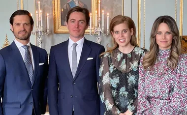 A group of four people dressed formally, smiling in a decorated room with candles and a portrait behind them.