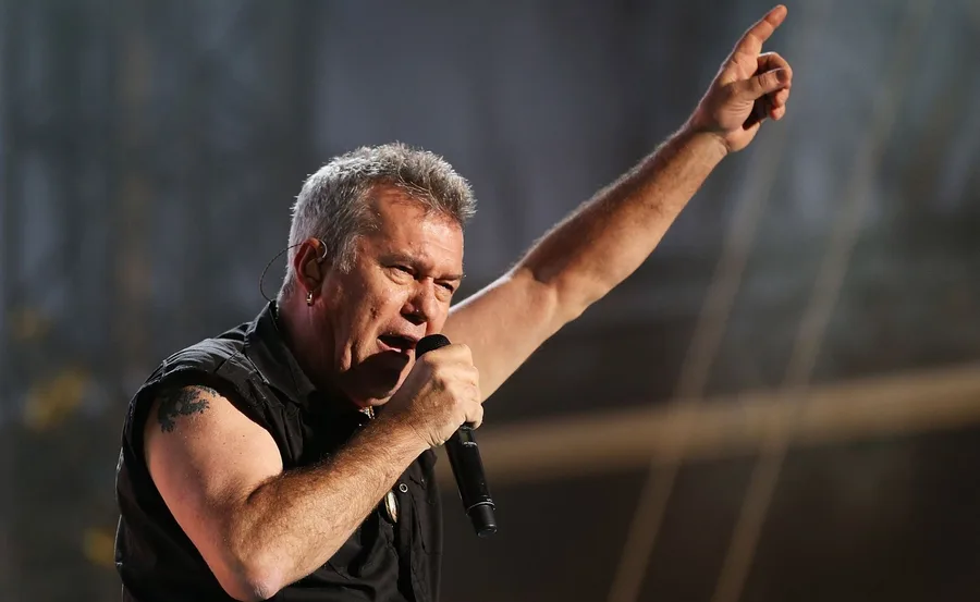 Singer performing passionately on stage, holding a microphone, with one arm raised.