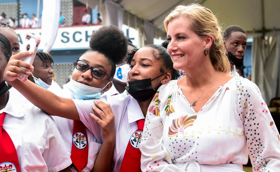 Group of students taking a selfie with a woman in a floral dress at a school event.