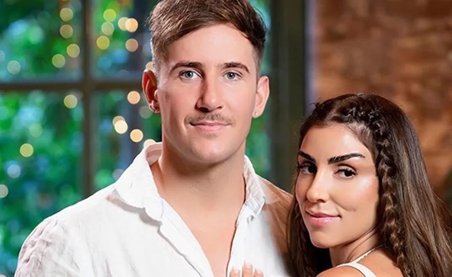 A couple posing together indoors, smiling, with a bokeh background.