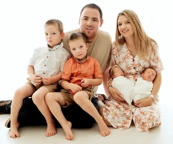 A family portrait with parents holding newborn twins and two older children sitting in front.