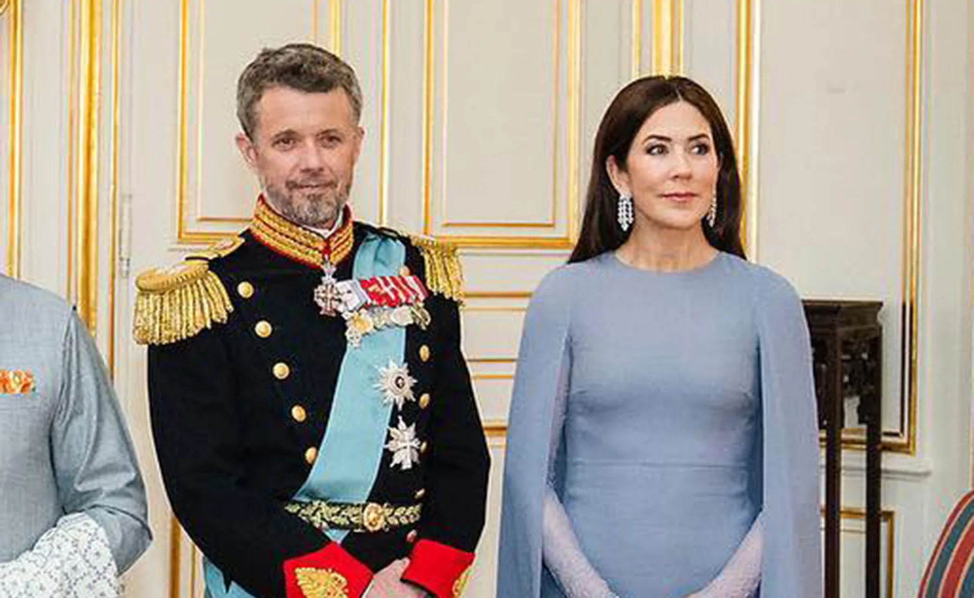 Formal event with woman in blue cape dress and man in military uniform; ornate room.