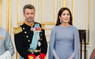 Formal event with woman in blue cape dress and man in military uniform; ornate room.