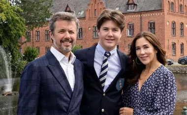 A family stands together smiling, with a brick building in the background.