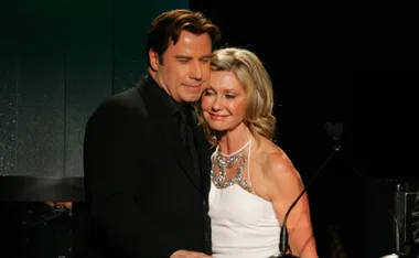 Couple embraces warmly at a formal event, woman in white dress, man in black suit.