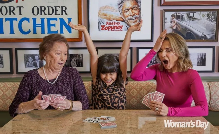 Three people playing cards at a table; the child raises arms in celebration, while the two adults look surprised.