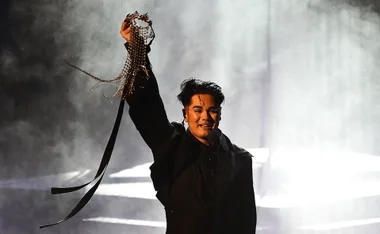 Sheldon Riley on stage at Eurovision Australia Decides 2022, holding a mask, in a dramatic light.