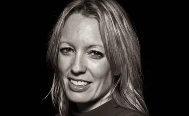 Black and white close-up portrait of a smiling woman with medium-length hair against a dark background.