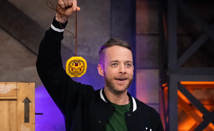A person holding a LEGO trophy on a stage, looking happy and excited.