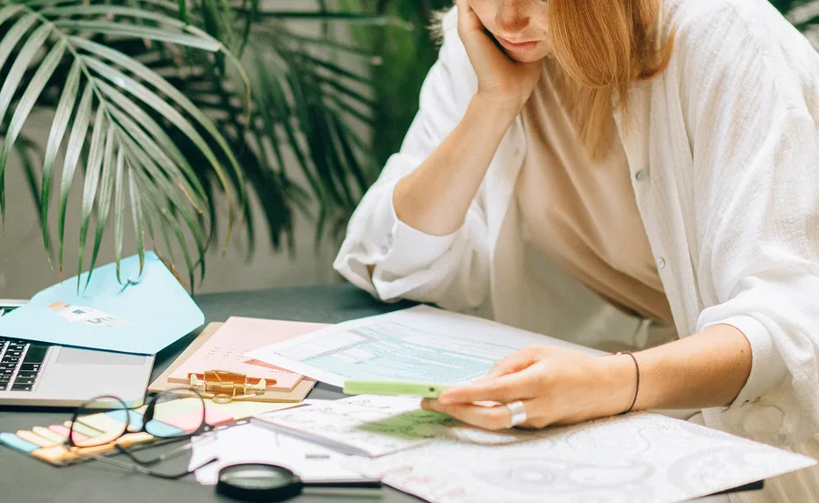 Person reviewing financial documents with a phone, laptop, and paperwork on a desk.