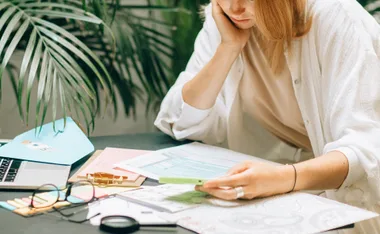 Person reviewing financial documents with a phone, laptop, and paperwork on a desk.