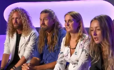 Contestants from Big Brother 2022 sit together on a couch, looking towards the camera with attentive expressions.