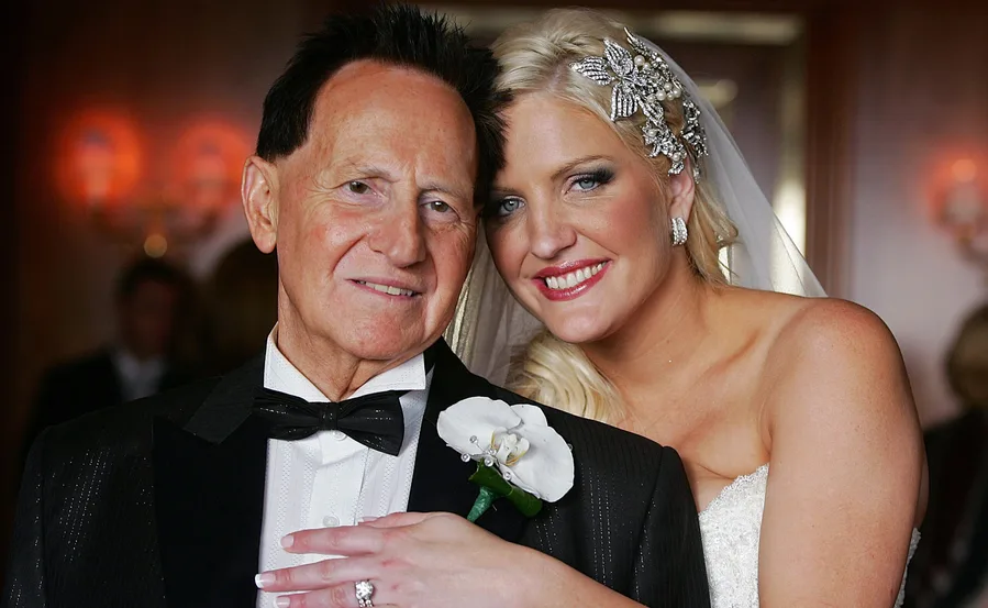 Bride in white gown and jeweled headpiece smiles, embracing an elderly man in a tuxedo with a white flower boutonniere.