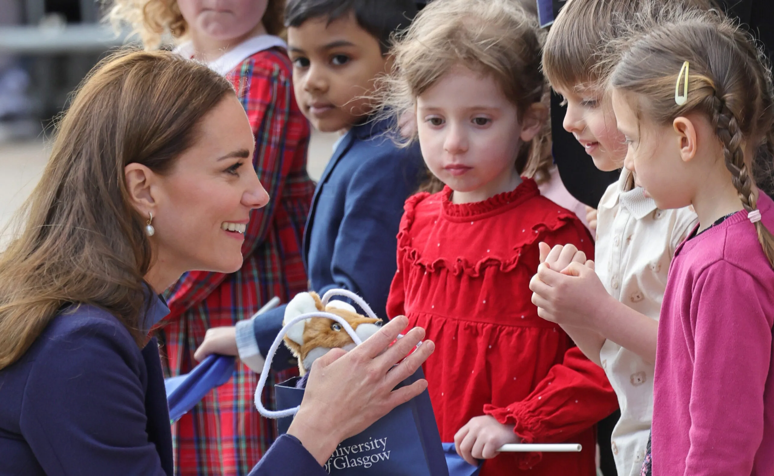 Kate Middleton smiling and interacting with children in Scotland, holding a gift bag.