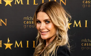 ```plaintext
Person with long blonde hair smiling at a 'Hamilton' themed event backdrop.
```