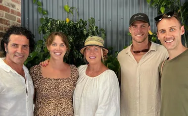 A group photo of five people smiling, with plants and a corrugated metal wall in the background.