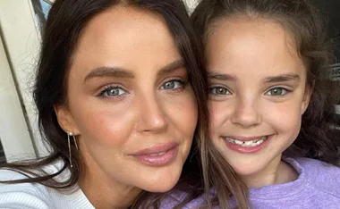 Mother and daughter smiling closely together, capturing a joyful moment with bright eyes and natural makeup.
