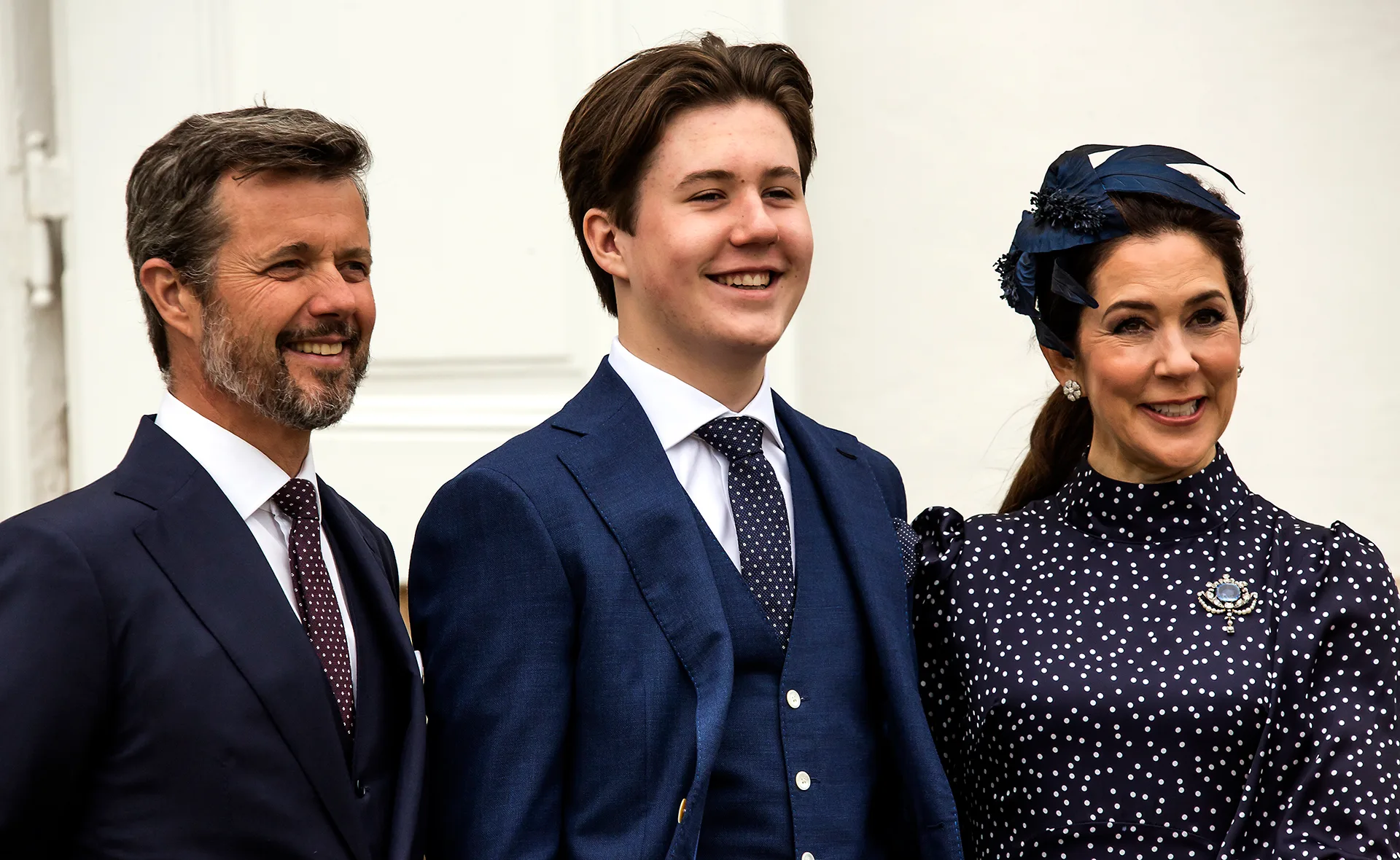 Three people smiling, dressed in formal attire, with a white background.