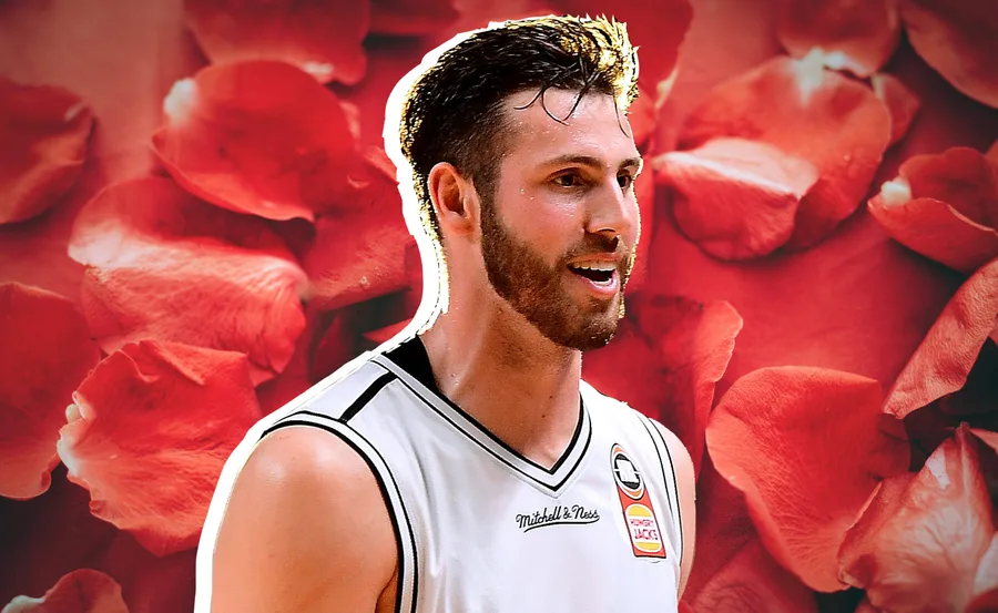 A man in a basketball jersey smiles against a background of red rose petals.