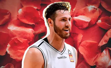 A man in a basketball jersey smiles against a background of red rose petals.