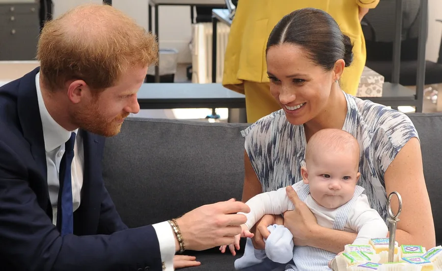 A man and woman smiling at a baby seated on her lap, with cupcakes nearby on a table.