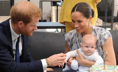 A man and woman smiling at a baby seated on her lap, with cupcakes nearby on a table.