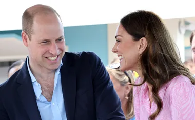 Prince William and Kate Middleton smiling and holding hands at a public event.