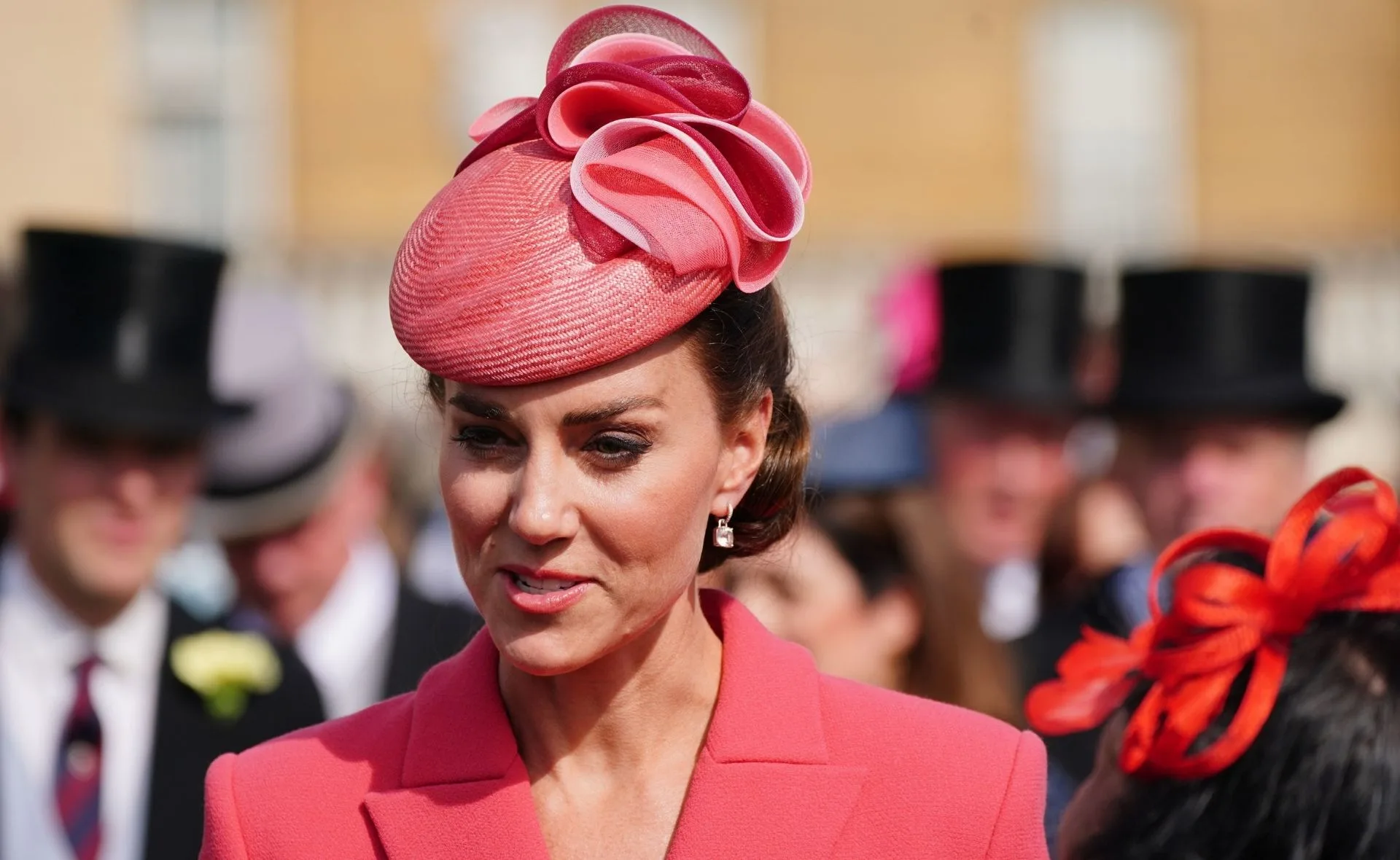Woman in a coral dress and hat at an outdoor event.